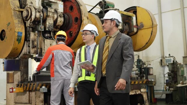 Factory audit narrows to two men whose hard hats lean close over the press mechanism they are studying together