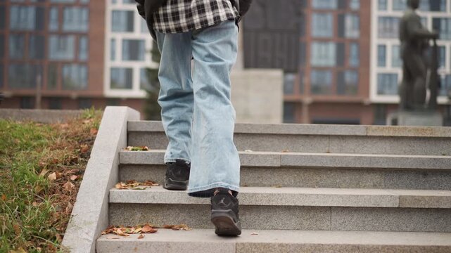Close up of person legs and feet as they walk down stone steps in urban environment. person wears light blue jeans black shoes with visible tread and scene includes scattered autumn leaves