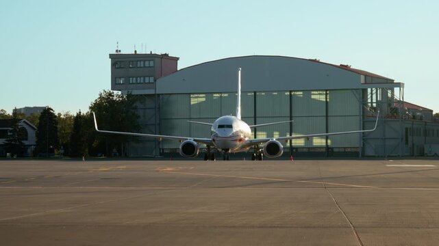Commercial passenger airplane stands on an airport tarmac near an aircraft hangar. Modern airliner prepares for departure. Civil aviation, global air travel, and transportation industry concept.