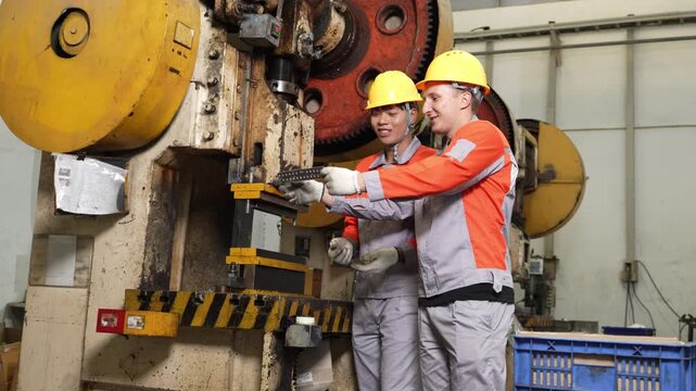 Factory audit weighs a stamped part as it passes between two workers standing beside the tall mechanical power press