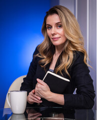 Obraz premium Emotions of a young business woman at her desk in a jacket on a light background drinking coffee