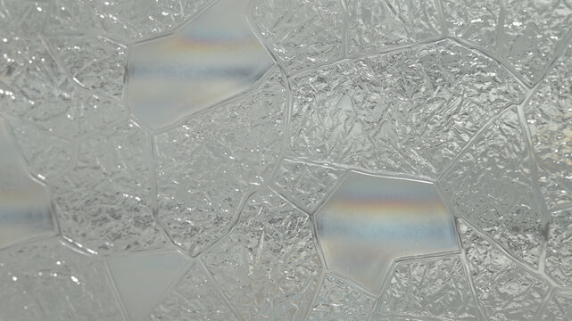 Close-up of translucent textured privacy window film with an irregular decorative glass pattern and subtle rainbow reflections, creating an abstract bright background.