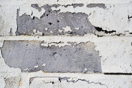 Peeling white paint on grey breeze block wall texture background with heavily distressed weathered surface