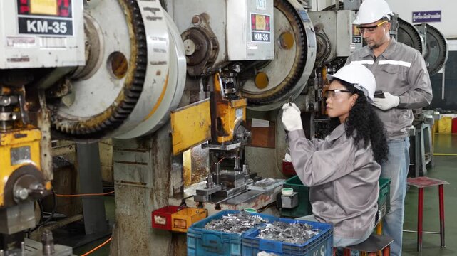 Steady press stamping runs along the line as two workers keep the machine fed and the parts crate slowly filling
