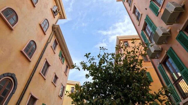 Wide shot of Italian-style residential houses with orange facades and green wooden shutters on Phu Quoc island, Vietnam, under a blue sky with a large tree.
