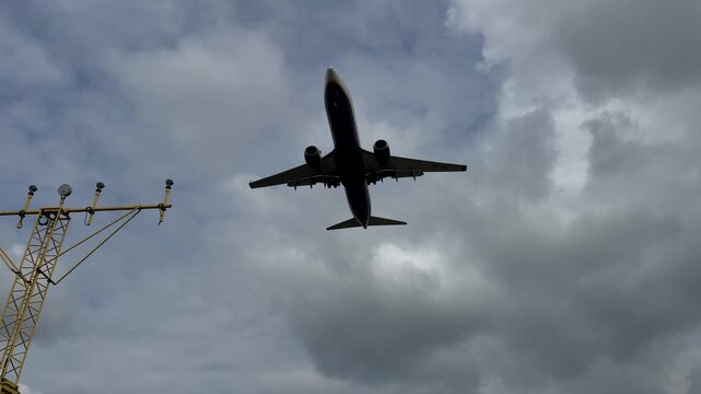 Commercial passenger jet captured from below while descending for landing against a blue cloudy sky. Aviation, air travel, airport approach, transportation, flight safety and modern aircraft.