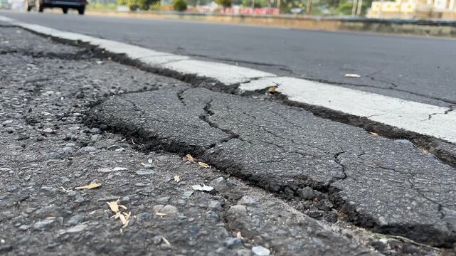 Damaged crack on asphalt street surface near road marking, close up view
