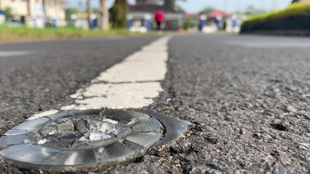 Broken cat eye road reflector embed on asphalt pavement line, low angle shot