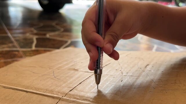 Close up child hand poking cardboard with pen tip, creative playing process
