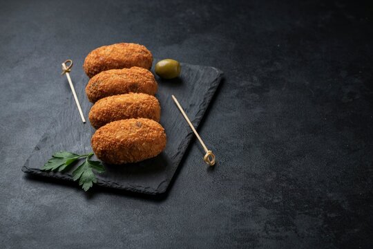 Crispy fried croquettes on a slate board with olives and parsley garnish