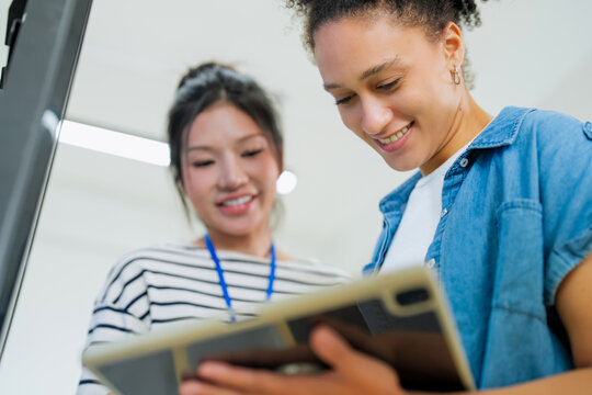 Two colleagues looking closely at a tablet screen, discussing intently from a dramatic low camera angle in a bright office setting.