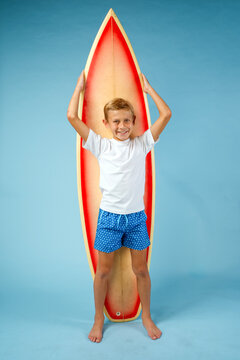 Smiling boy wearing vintage swim trunks standing in front of a surfboard