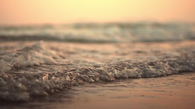 Close up of gentle ocean waves washing onto sandy beach in warm golden sunset, peaceful seascape with shallow water and soft surf, tranquil coastal nature, summer travel and relaxation background