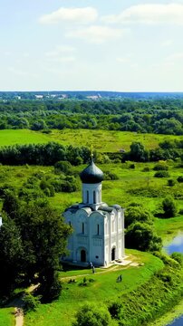 Vertical video. Russia, Bogolyubovo. Church of the Intercession on the Nerl, a white-stone Orthodox church with a single dark dome, Drone footage over the Nerl River floodplain in summer. Drone foota