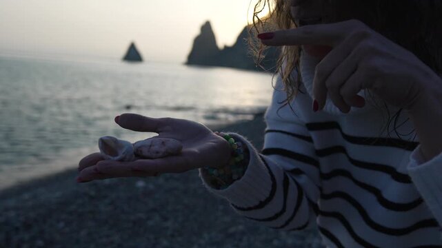 Woman, Shell, Sunset. Young female tourist holding a small seashell on a secluded beach cliff during a beautiful golden hour
