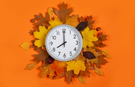 Top view of round analog clock showing eight o'clock surrounded by autumn foliage on orange background. Template for fall discount banners, evening deals, and time management.