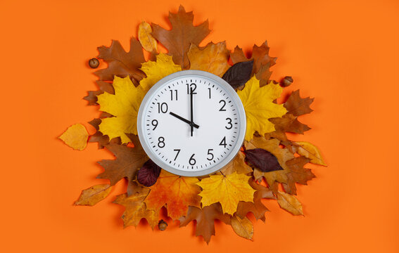 Top view: 10 o'clock, round wall clock on autumn leaves wreath over orange background, daylight saving time concept. Conceptual flat lay composition for transition of the fall season, time management.