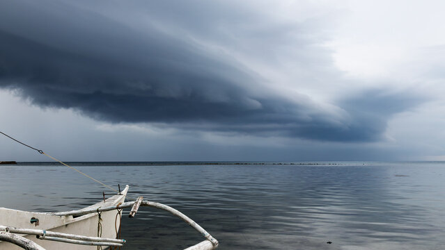 Dark Shelf Cloud Storm Front Approaching Over Coastal Sea and Traditional Outrigger Boat
