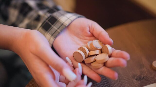 Close up of hands holding small round wooden objects fingers gently moving them. Hands with long nails interact naturally as scene remains focused on texture detail and soft lighting