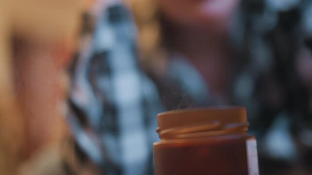 Close up of woman wearing glasses and plaid shirt resting her head on hand with orange prescription bottle in focus. Soft indoor lighting creates warm ambiance as subject remains still