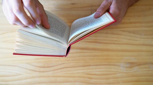 Top view shot of person reading book and scrolling through pages with hands
