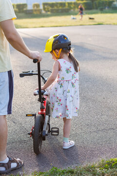 Father helping young daughter learn to ride bicycle outdoors