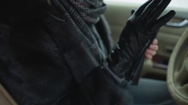 Close up of woman in black leather gloves and fur coat inside car adjusting her gloved hands. scene shows interior with soft lighting focusing on texture details like glove material