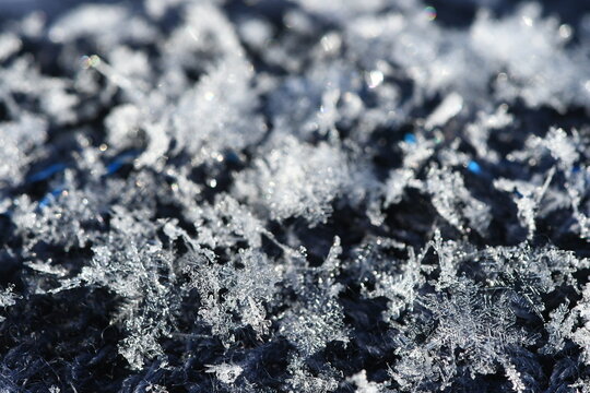 Horizontal macro photograph of delicate crystal snowflakes with detailed hexagonal structure resting on navy black knitted fabric