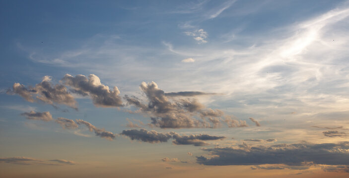 Soft clouds drifting across a blue evening sky with warm sunlight, creating an expansive atmospheric background with delicate cloud formations and natural beauty.