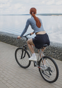 Young sportswoman riding a bicycle along a waterfront promenade. Outdoor cycling, exercise, recreation and active healthy lifestyle in a scenic setting.