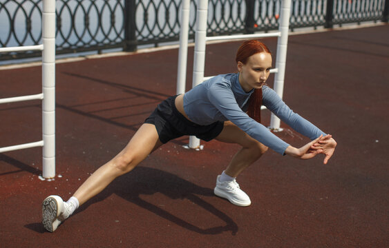 Young woman performing a deep side stretch on a waterfront promenade. Outdoor exercise, flexibility training, warmup and active lifestyle concept.
