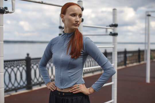 Young woman standing confidently on a waterfront promenade, looking right side. Fitness, wellness, strength and active lifestyle concept.