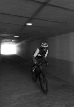 Black and white photo of a cyclist riding through a tunnel road with a blurred background