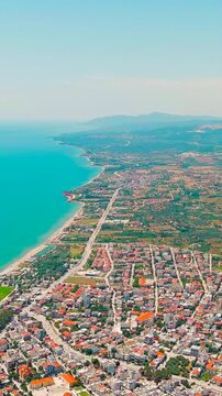 Vertical video. Alexandroupolis, Greece. Aerial panorama of the Thracian Sea coastline, dense terracotta rooftops and the historic 1880 lighthouse at the harbor entrance. Drone footage. Rich colors