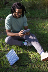 Adult African man sitting on grass using tablet while charging via solar panel and power pack © WavebreakMediaMicro
