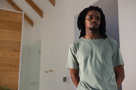 African man wearing light green Tshirt standing right of modern interior by glass shower