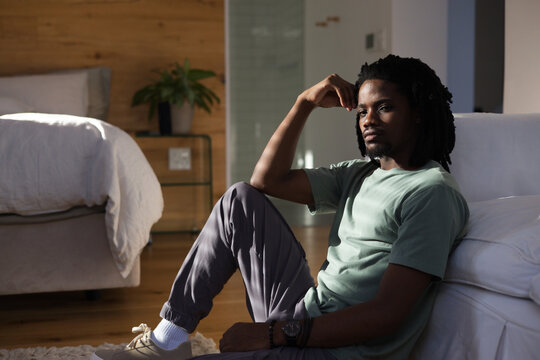 African American man sitting on wooden floor in modern bedroom wearing sneakers and wristwatch