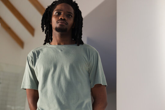 Adult African man standing at home under exposed beams in light green T-shirt by glass tiles