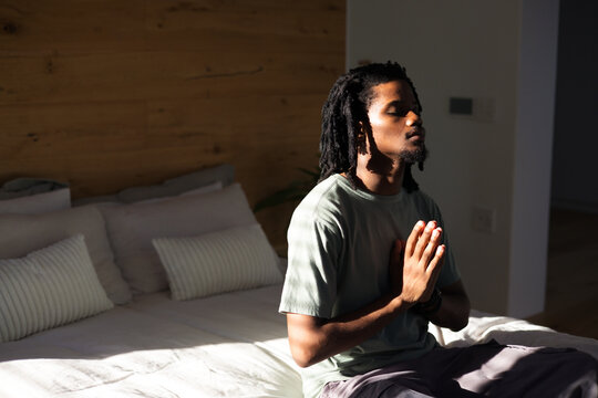 African American man sitting on bed edge in bedroom, in green tee, checking wristwatch, copy space