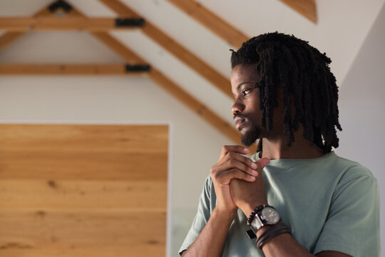Adult African American man standing clasping hands near chest in loft showing wristwatch