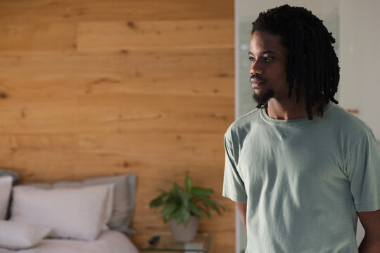 African American man standing hands behind back gazing right in bedroom by bedside table