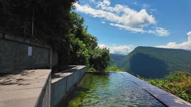 A tranquil infinity secret pool in Georgia in Racha with clear water reflecting the blue sky, located on the mountainside with stunning panoramic views of the green valley