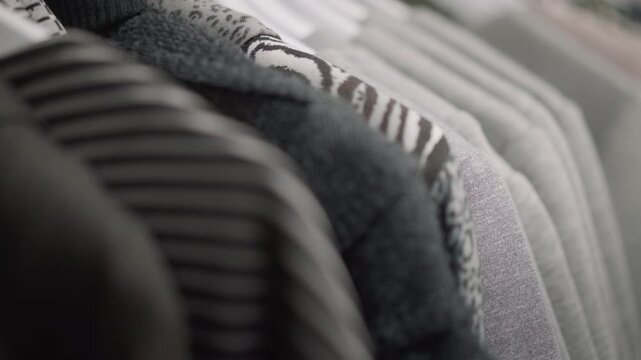 Close up of various clothing items hanging on rack showcasing different textures and patterns. Soft lighting highlights fabric details like stripes animal prints knitwear texture soft