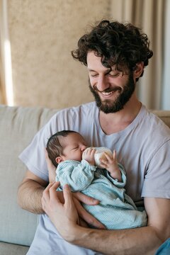 Young father feeding newborn with a bottle on a sofa for parenting banner and family lifestyle background