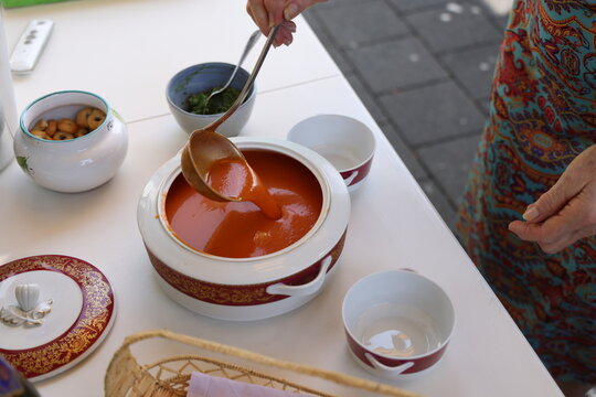 Une femme &acirc;g&eacute;e sert une soupe de tomate &agrave; la louche en ext&eacute;rieur
