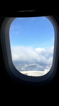 Airplane window captures the evolving view from clouds to clear blue sky, illustrating the journey through different altitudes and weather