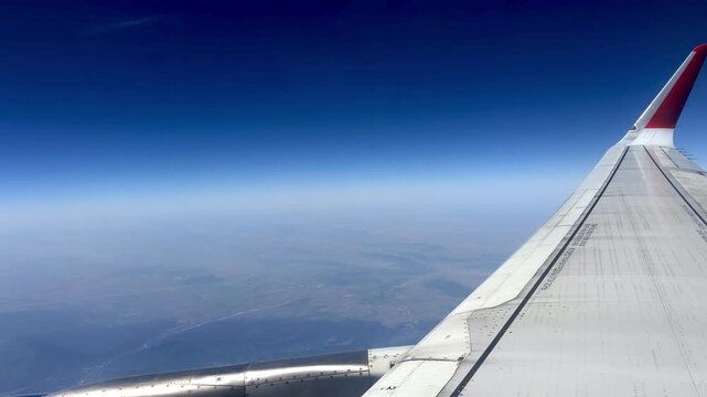 Aerial perspective from airplane window reveals aircraft wing with clear blue sky and expansive land below, illustrating the journey of flight