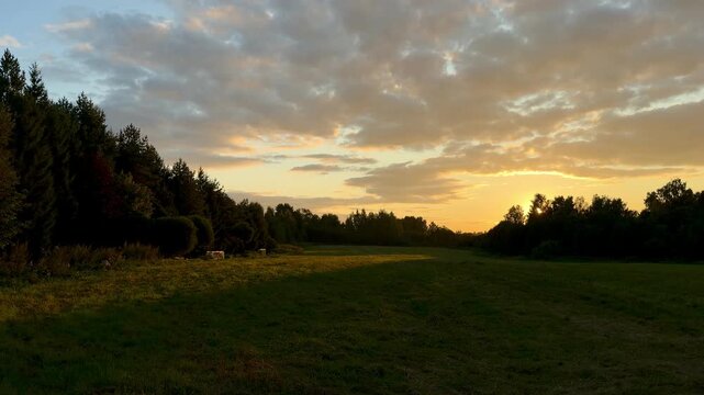 Scenic view of a sunset illuminating a grassy field, with trees on the horizon and a gradual change in light and color across the sky