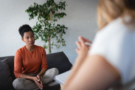 Female therapist listening and taking notes while a woman rests on a sofa and talks during an individual psychotherapy session