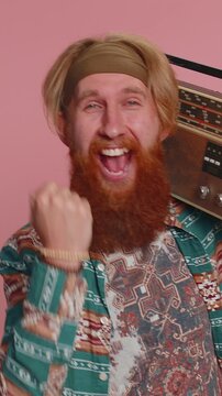 Hippie redhead man using retro tape record player to listen music, disco dancing of favorite track, having fun, entertaining, fan of vintage technologies. Hipster ginger bearded guy on pink background